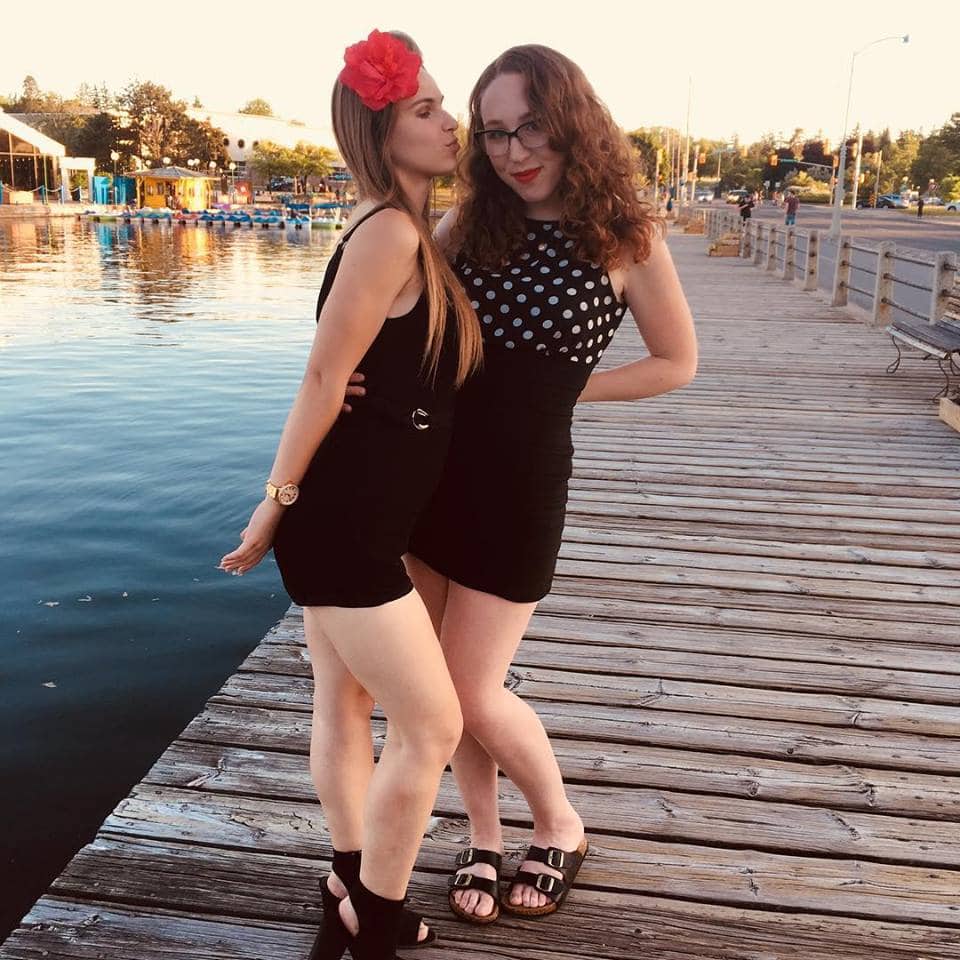 Two girls, standing by the water. 