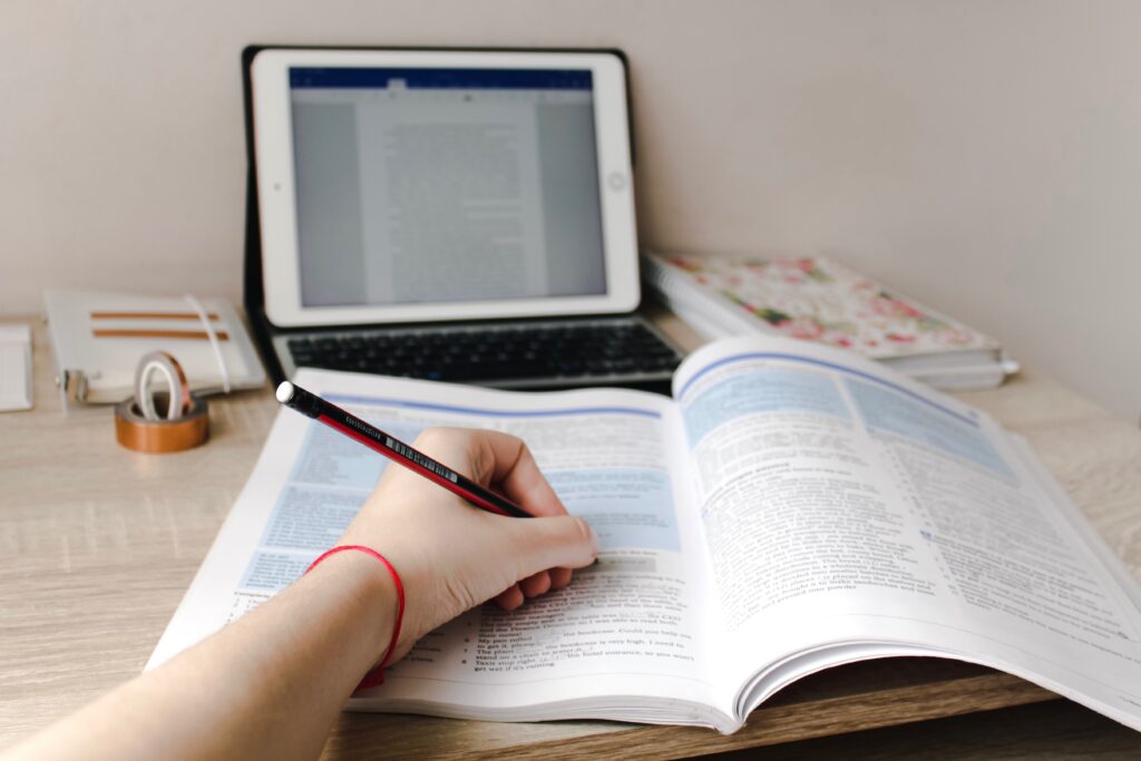 How to save money on textbooks - woman writing in open book with laptop open