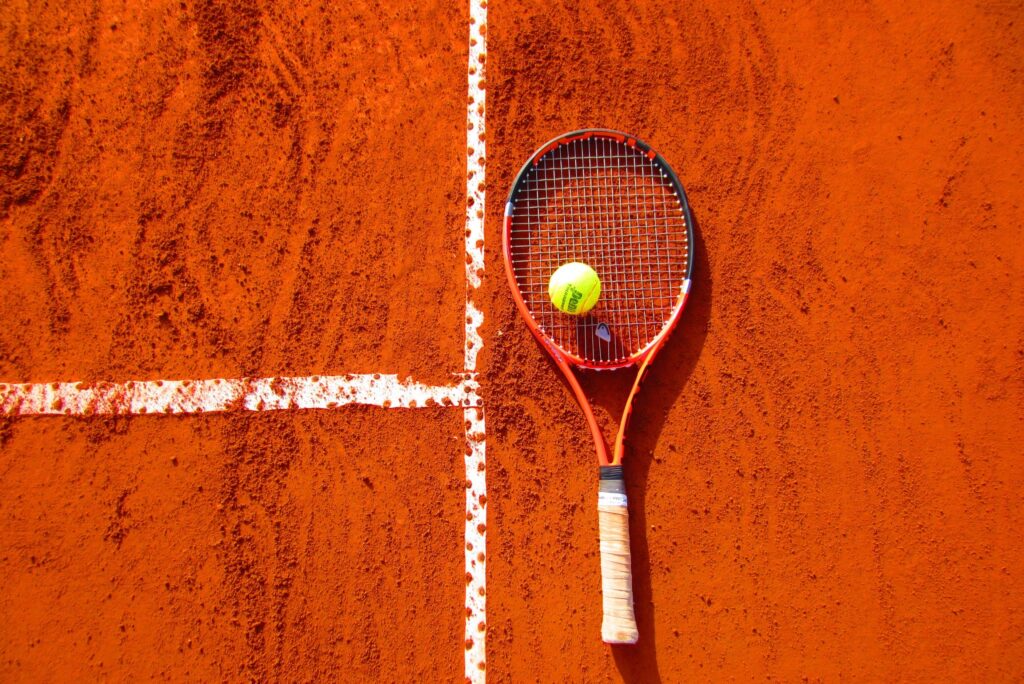 Tennis racquet and ball on orange tennis court.