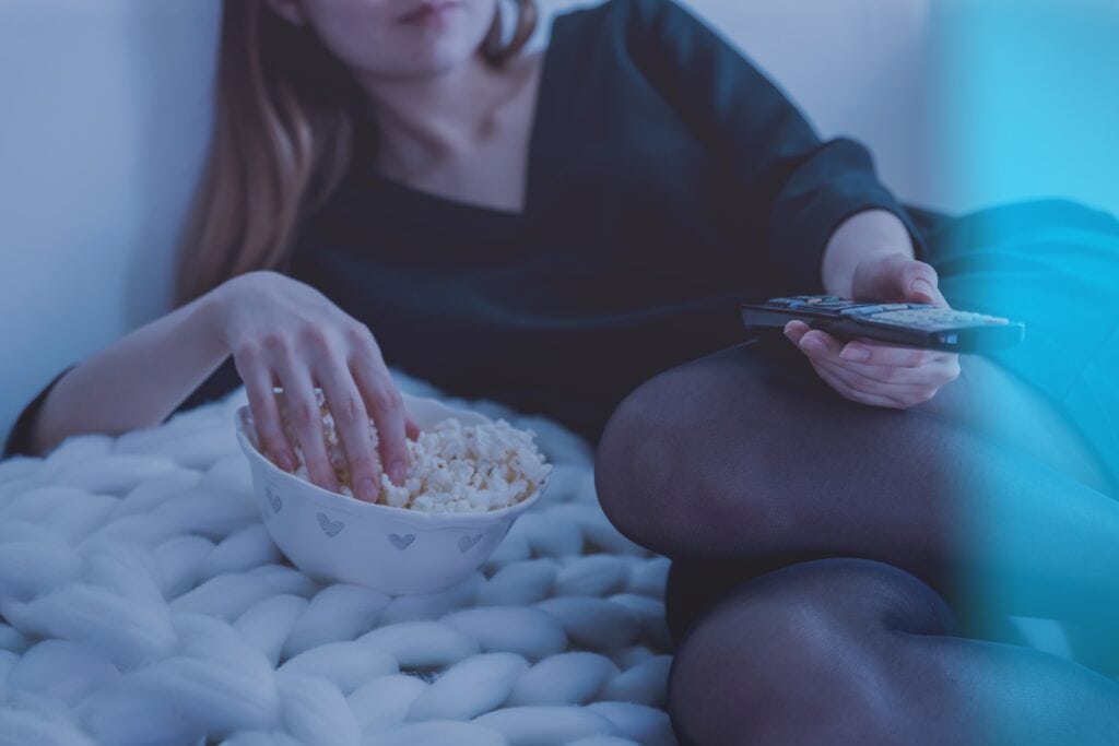 Woman sitting on bed eating popcorn for scary movie marathon