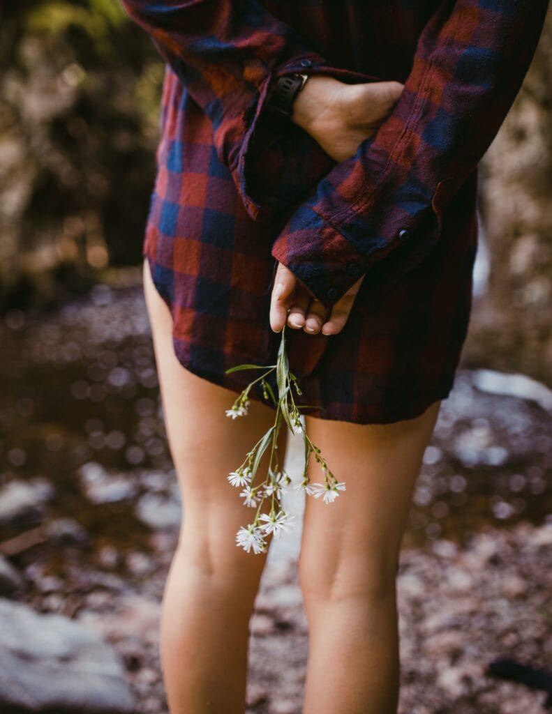 Girl wearing a flannel holding a flower behind her back.