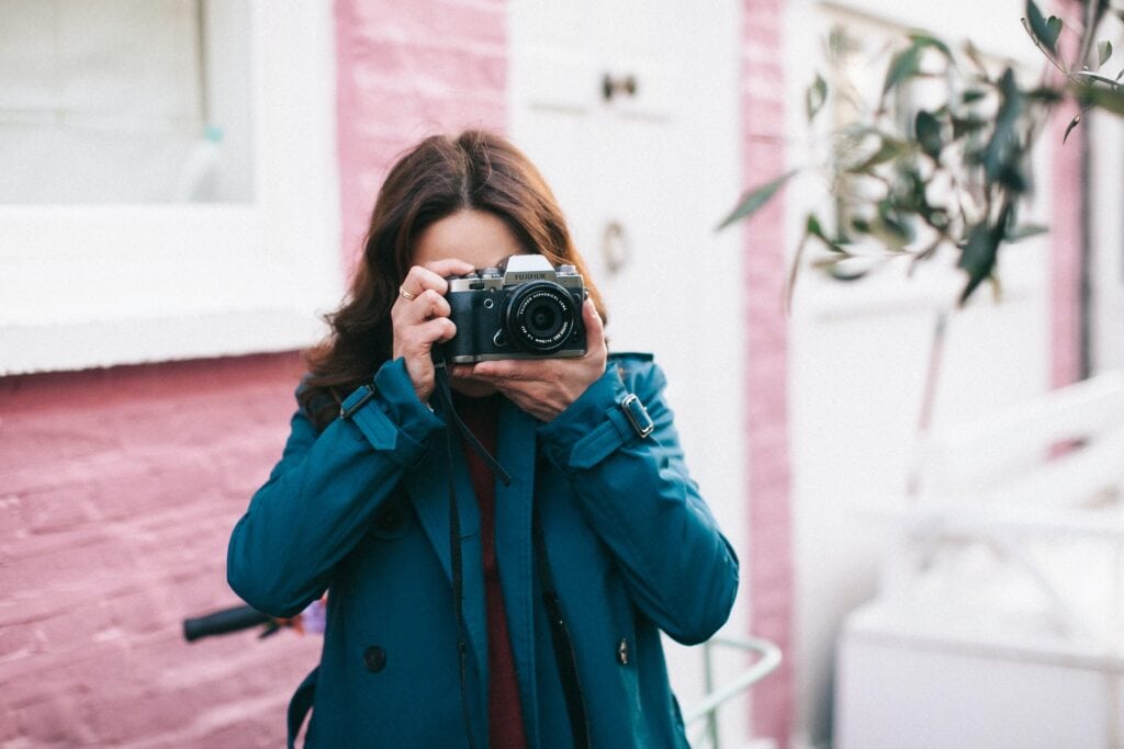 Girl with camera in front of pink house.