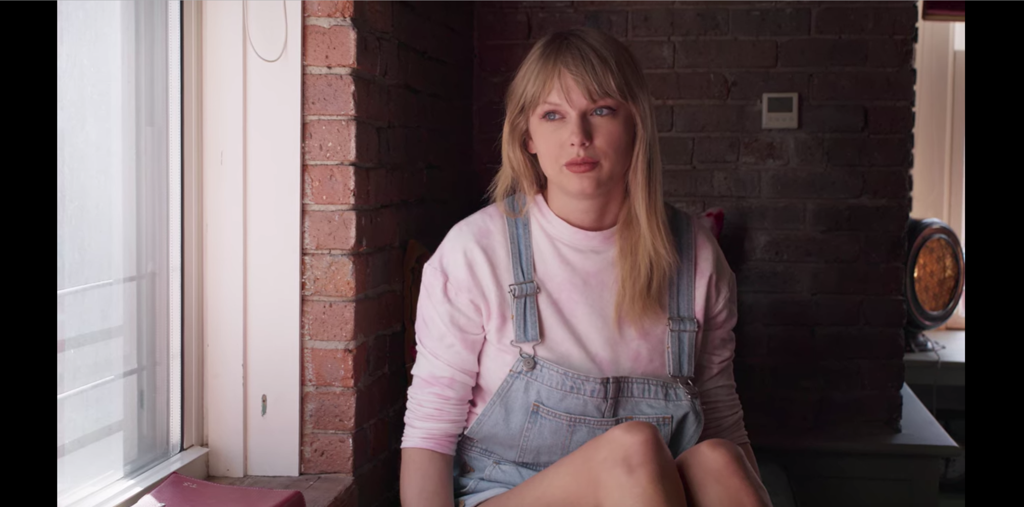 Taylor Swift in Miss Americana wearing a pink sweatshirt and overall shorts
