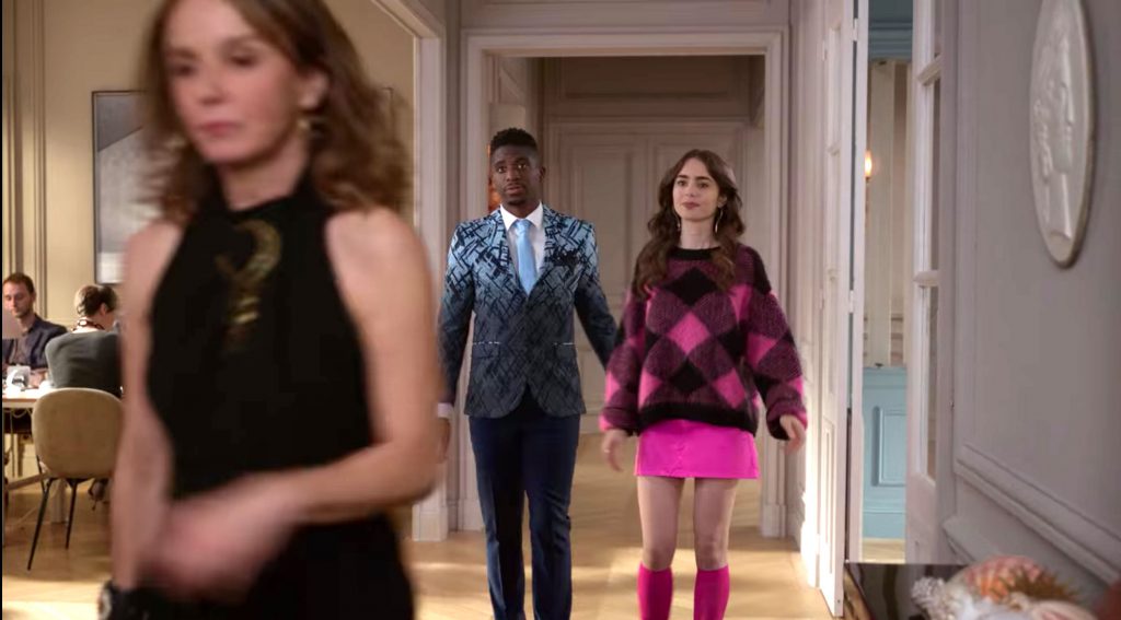 Emily in Paris fashion guide - photo of emily in a Pink outfit with pink mini skirt, plaid sweater, and pink socks and heels