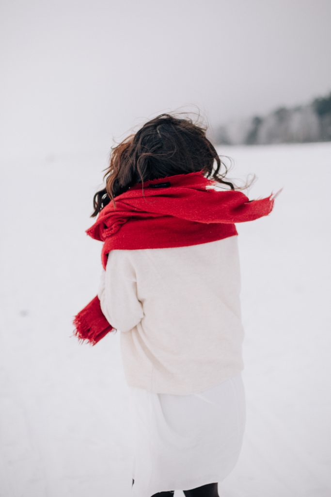 Woman wearing white in the snow with a red scarf, holiday style tips