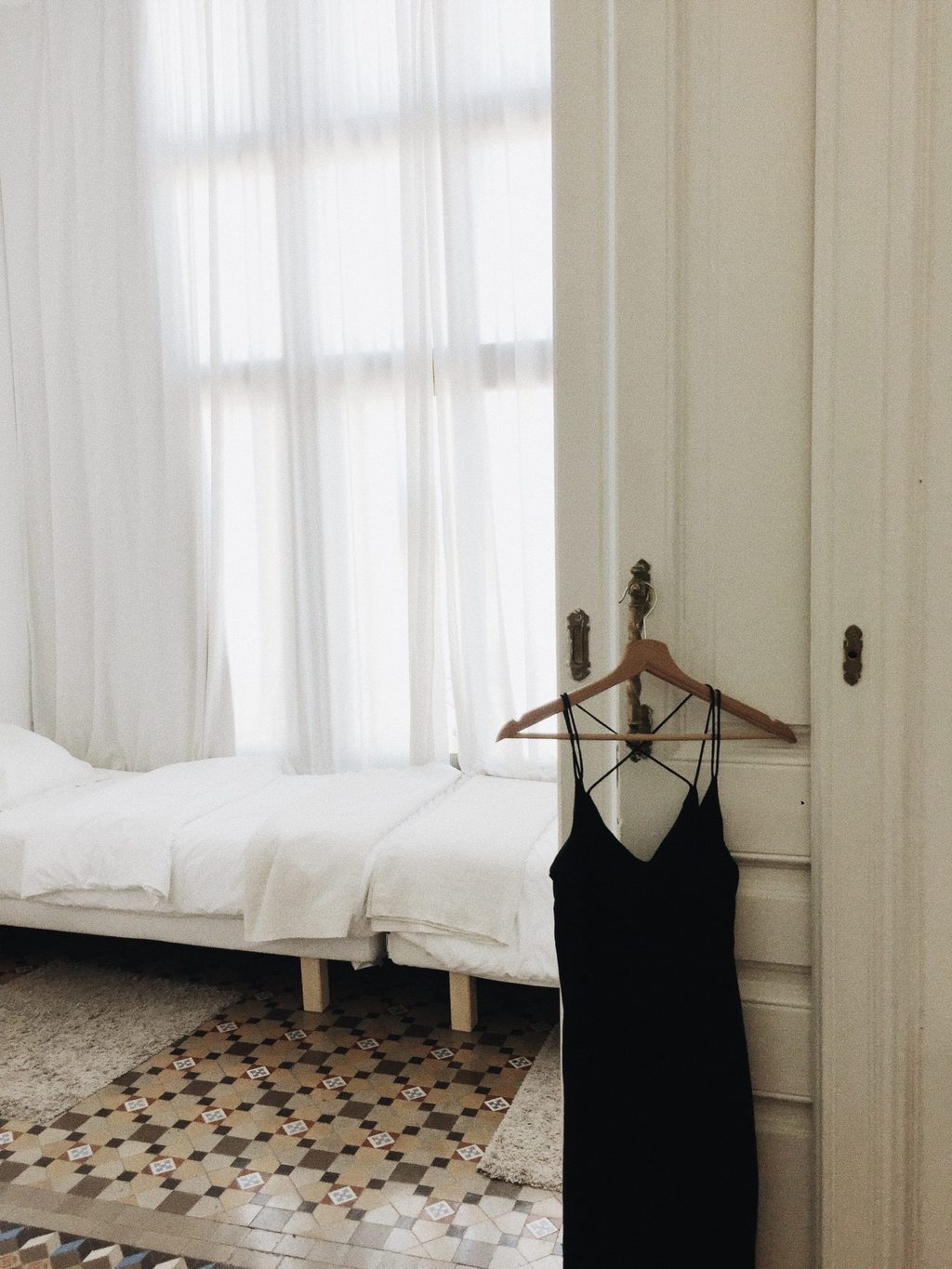 Little Black Dress hanging on a hanger on a door with a white bed in the background