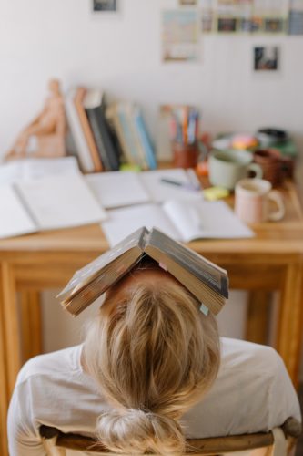 Photo of a person with a messy desk and a book on their head, college organization tips.