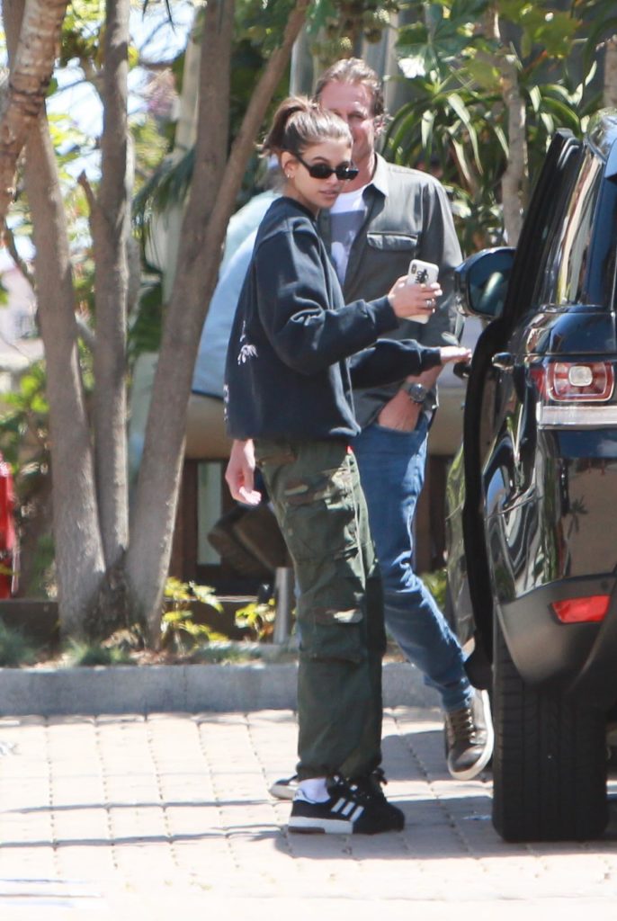 Kaia Gerber wearing a black hoodie, green army cargo pants, and black Addias sneakers