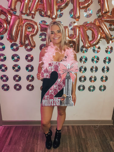 Photo of girl holding a 21 sign with backdrop of CDs