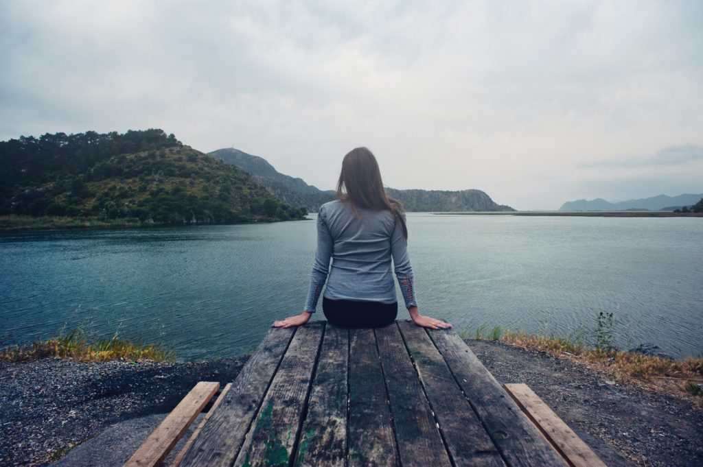 A girl sitting on a pier over-looking a river.