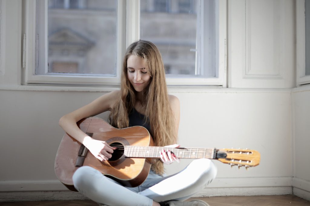 A girl sitting on the floor playing guitar.