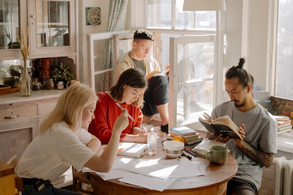 Four people at a desk, reading and studying.