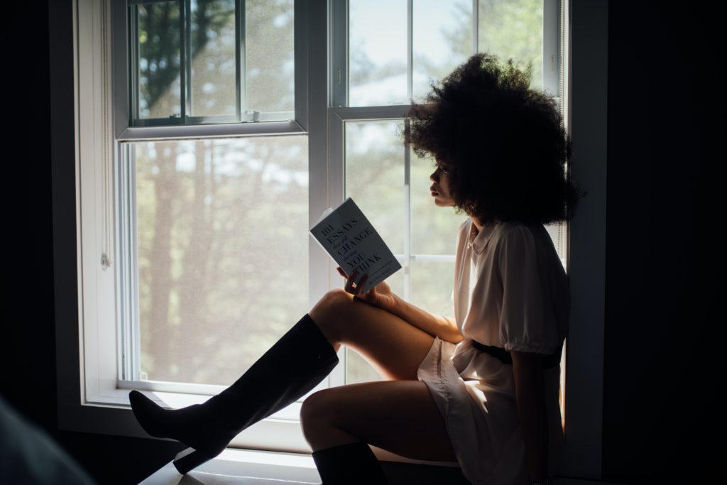 A girl sitting down by a window reading. 