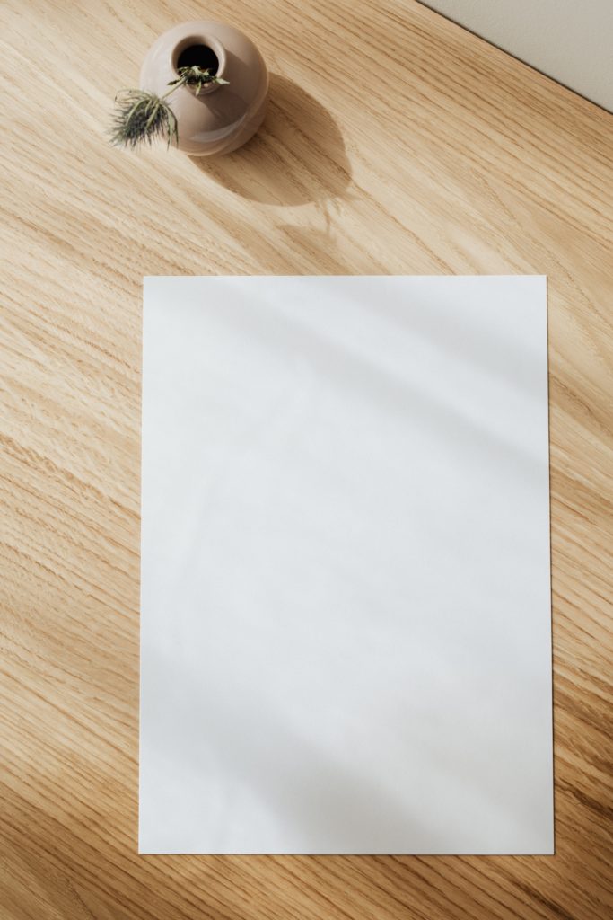 A blank A4 sheet of paper on a desk with a plant.