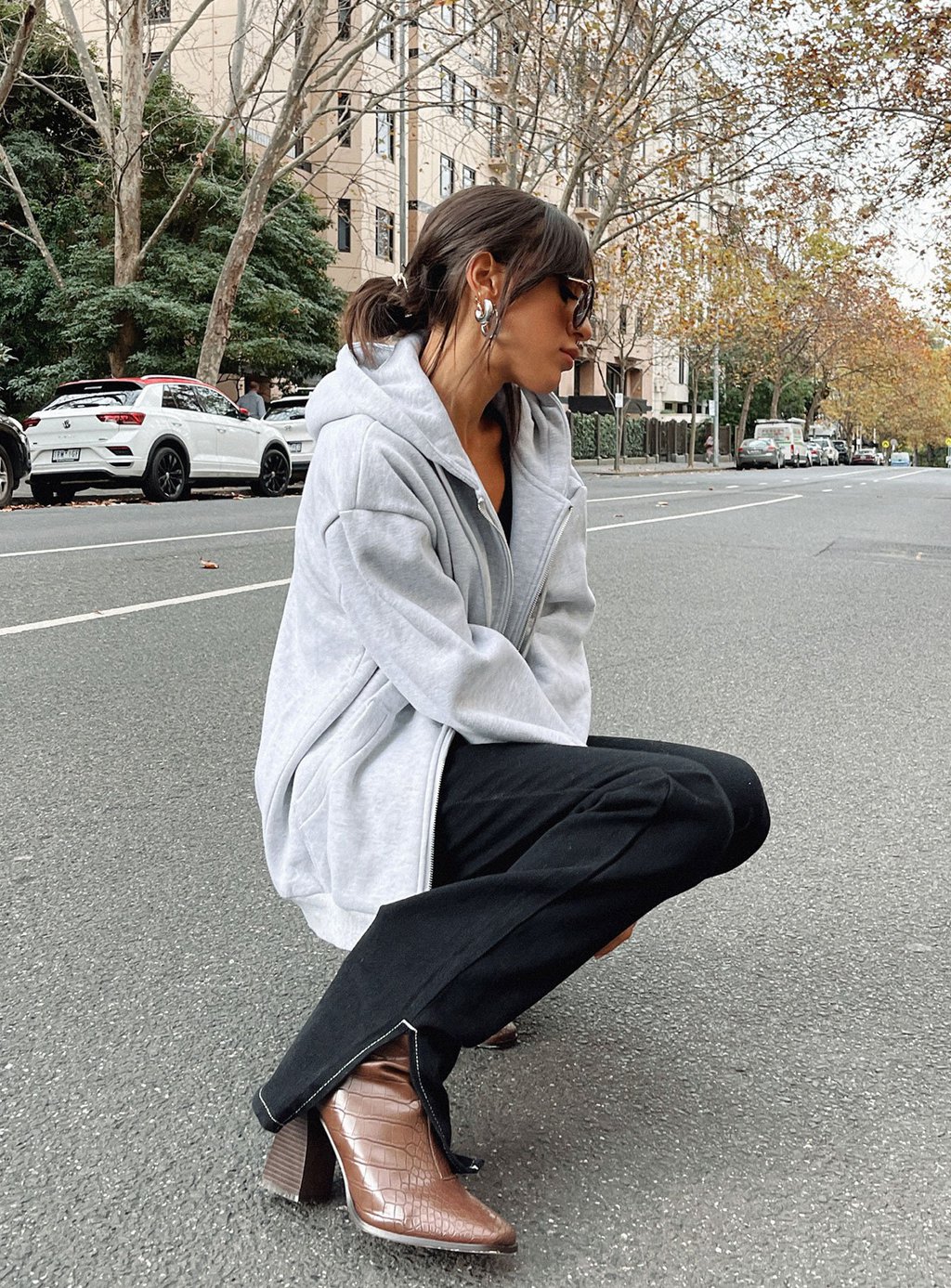 Photo from Princess Polly of a woman wearing fall wardrobe essentials including brown leather boots, flared pants, and a zip sweatshirt