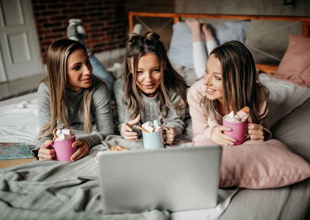 Three women watching a show on a laptop while drinking hot chocolate - things to do over winter break