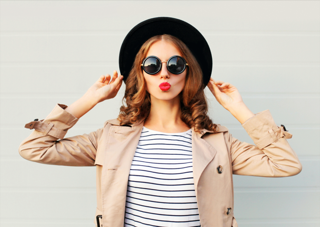 Woman wearing a black hat, trench coat, and white and black horizontal striped shirt with round sunglasses and pink lipstick - things to do over winter break