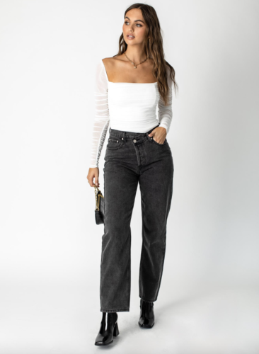 White square neck long sleeve top with sheer sleeves, high-waisted dark grey jeans, black ankle boots with chunky heels.