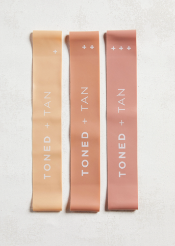 Photo of three exercise bands in shades of blush pink with the text Toned + Tan written on them
