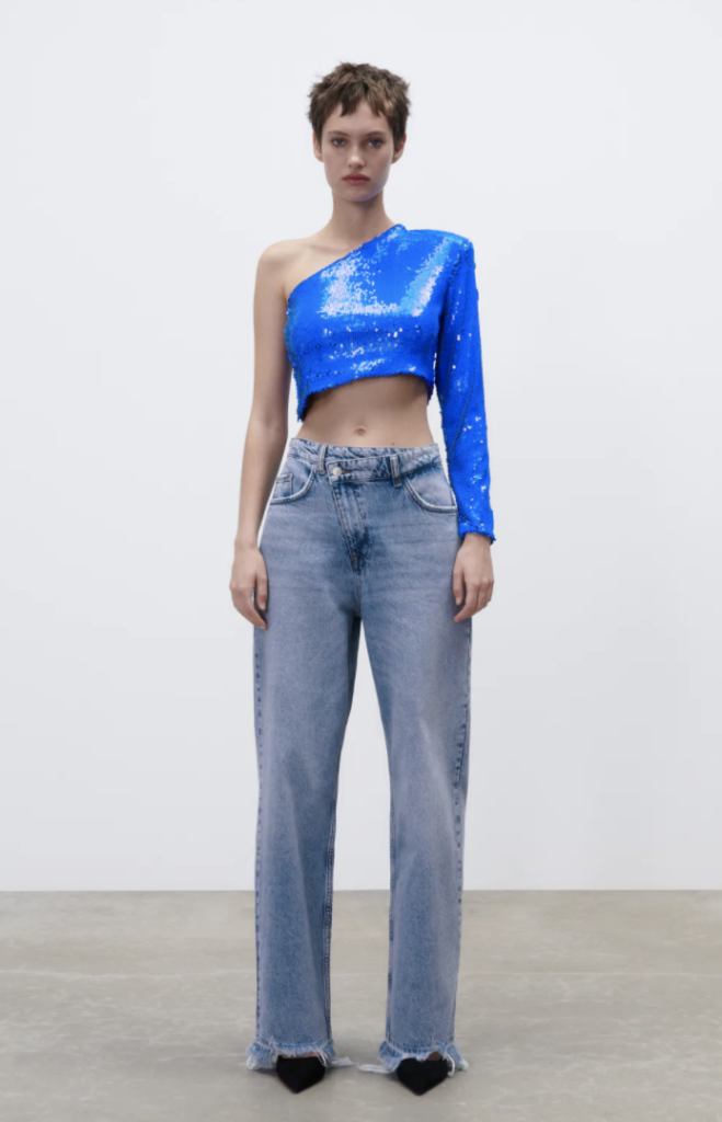 NYE outfit from Zara consisting of blue wide-leg jeans, cobalt blue sequin one-shoulder crop top, and black pointed toe ankle boots 