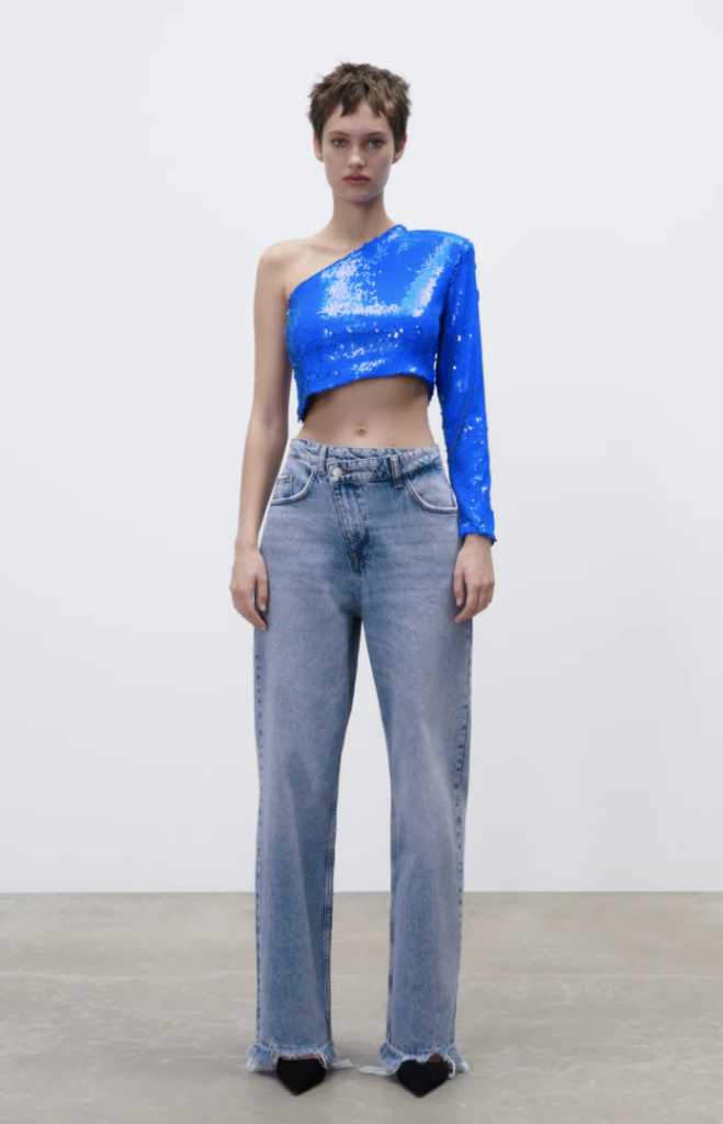 NYE outfit from Zara consisting of blue wide-leg jeans, cobalt blue sequin one-shoulder crop top, and black pointed toe ankle boots