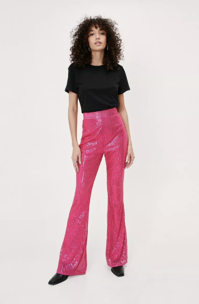 Photo of a model wearing pink sequin flare pants, a black t-shirt, and black booties