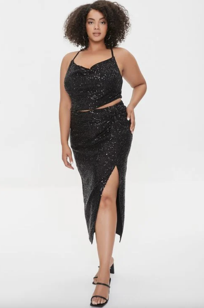 Plus size black sequin two piece dress for New Year's Eve with above-the-knee slit, calf length skirt, and spaghetti strap crop top, paired with strappy heels