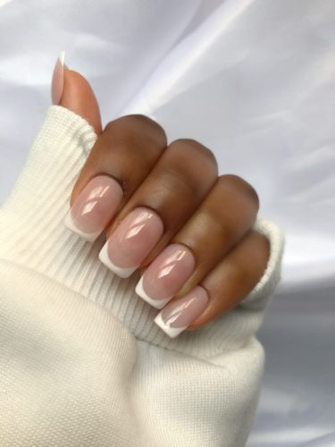 Classic french tip manicure shown on a woman with dark skin