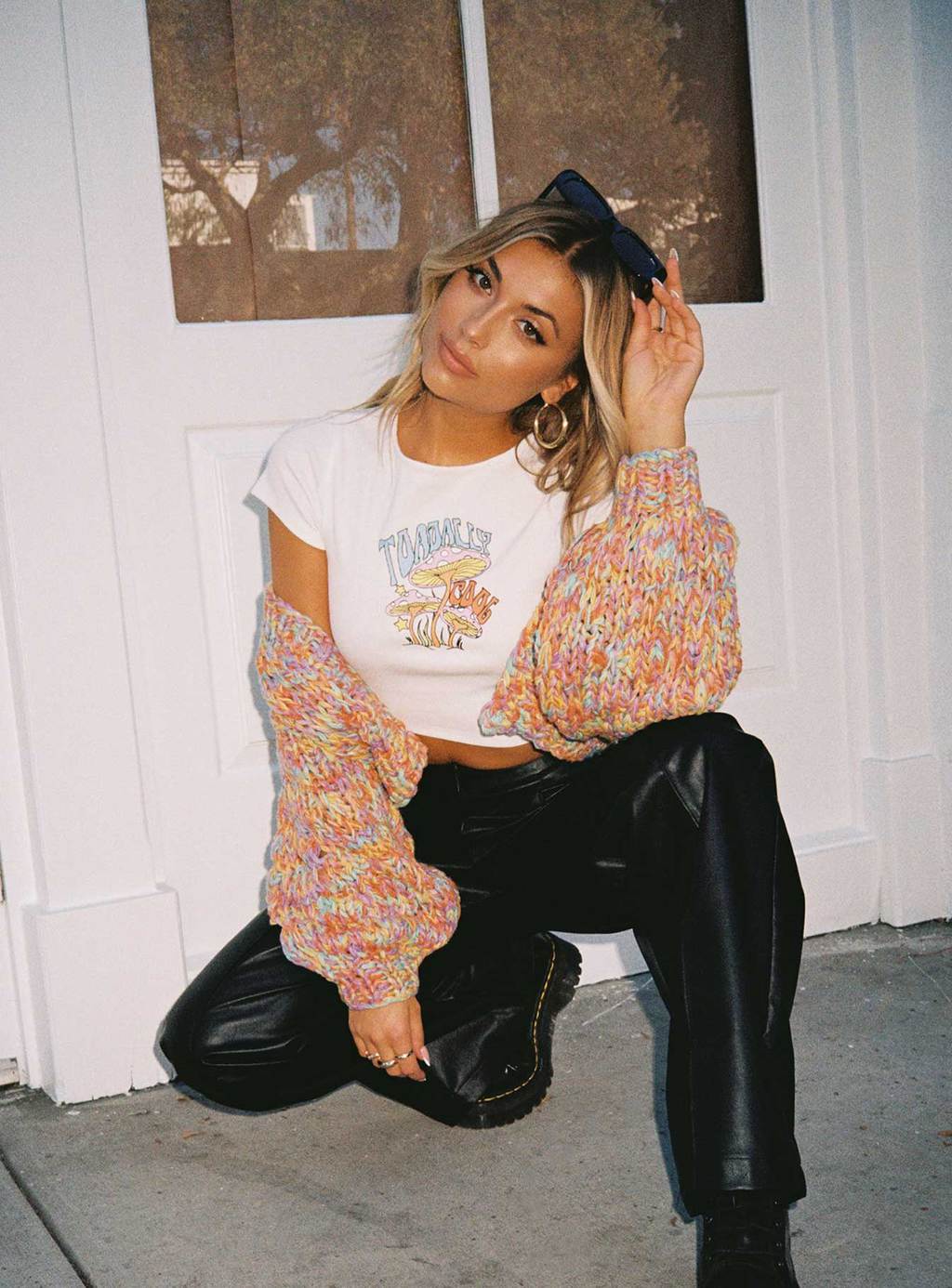 A woman sitting with her knees touching the elblow, wearing a Cropped Graphic Tee with Leather Pants and a Cardigan
