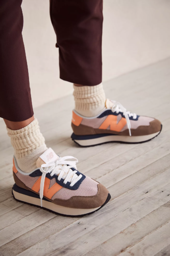 New Balance sneakers in brown, orange, and white, paired with high socks and brown pants