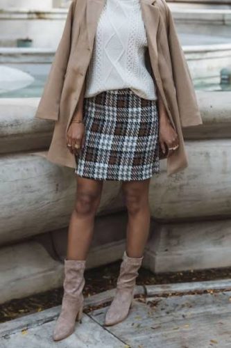 Classy winter outfit with plaid mini skirt, cable knit sweater in cream, camel coat, and brown suede ankle booties