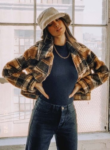 Cute winter outfit idea with black jeans, black bodysuit, black and brown shacket, light brown bucket hat, and gold chain necklace