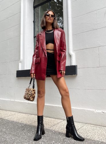Princess Polly Faux Leather Blazer in red paired with black cutout mini dress, black ankle boots, and fuzzy faux fur bag plus sunglasses and a chain necklace