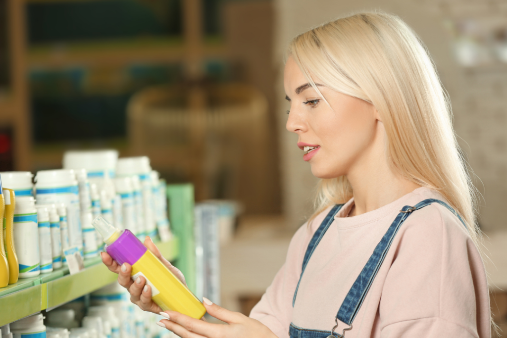 Blonde woman reading the ingredients on a bottle of purple shampoo