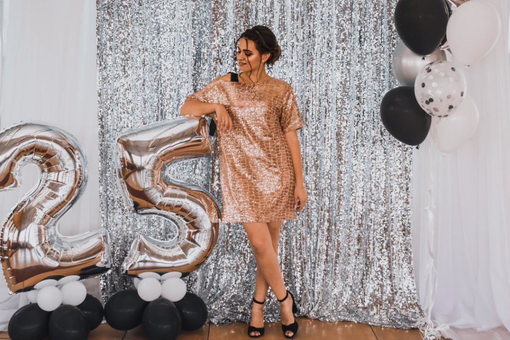 Photo of a woman on her 25th birthday wearing a pink sequin dress and standing next to silver balloons in the shape of the number 25
