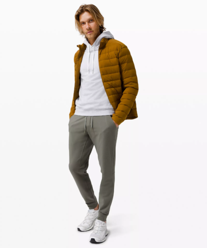 Photo of a man wearing gray lululemon joggers with a light gray sweatshirt and brown puffer coat, paired with sneakers
