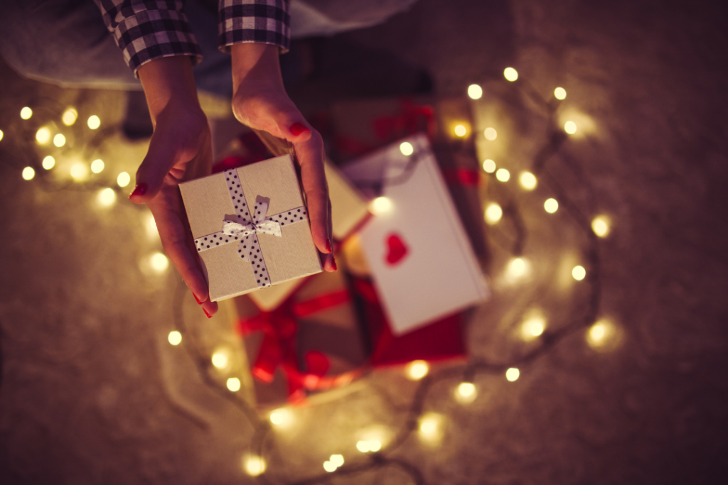 Photo of a woman holding a small box with a polka dot ribbon above a pile of Valentine's Day gifts