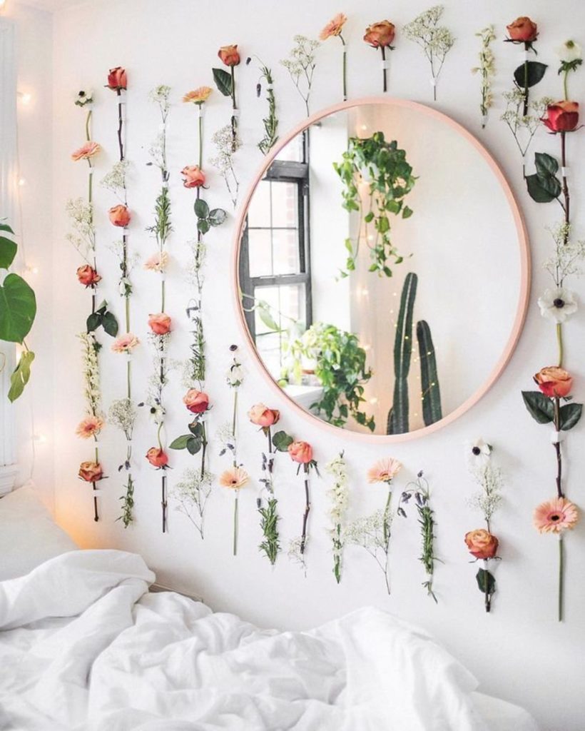 Roses and baby's breath flowers hung on the wall around a circular mirror in an aesthetic room