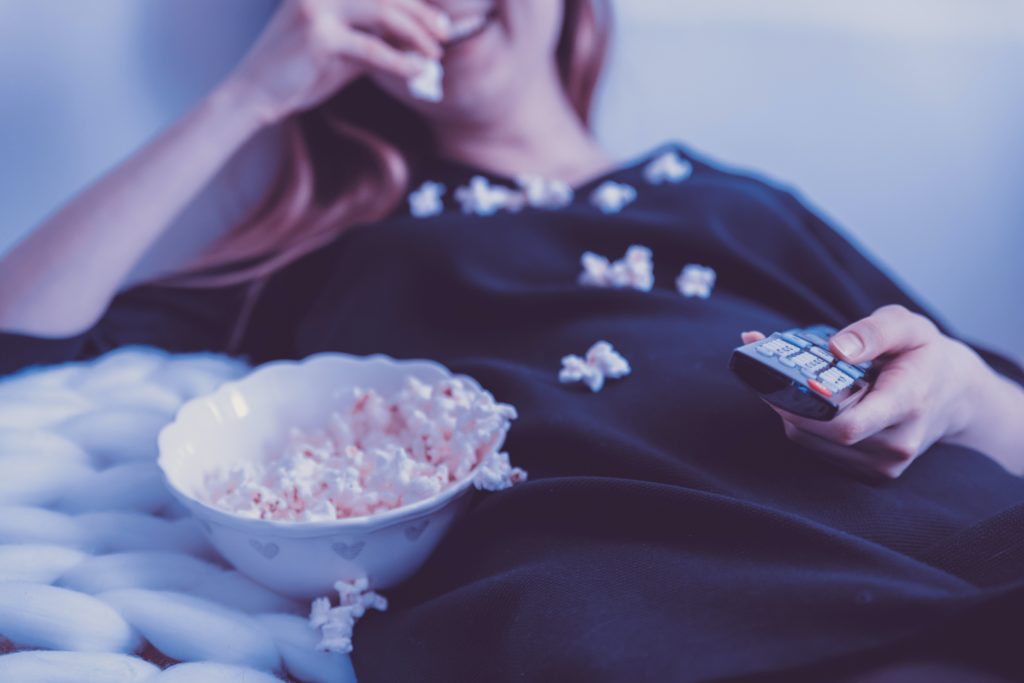 photo of a woman eating popcorn with a remote in her hand from unsplash