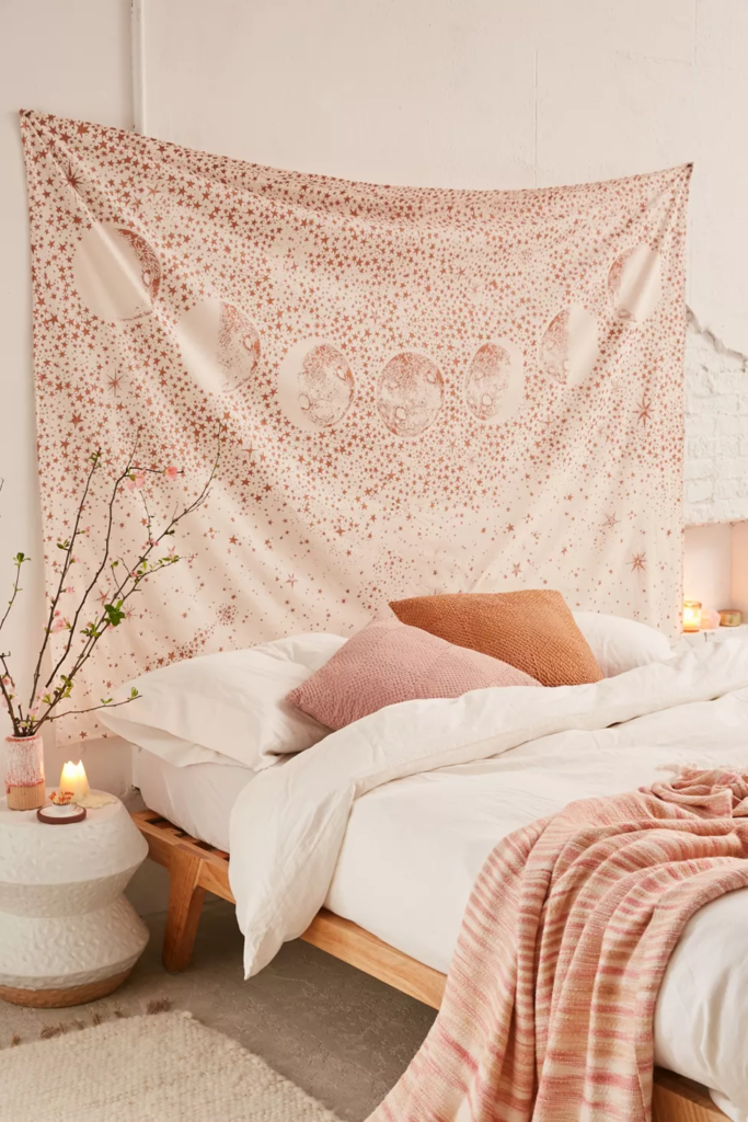 Large pink and beige tapestry used as a headboard in a pastel aesthetic room