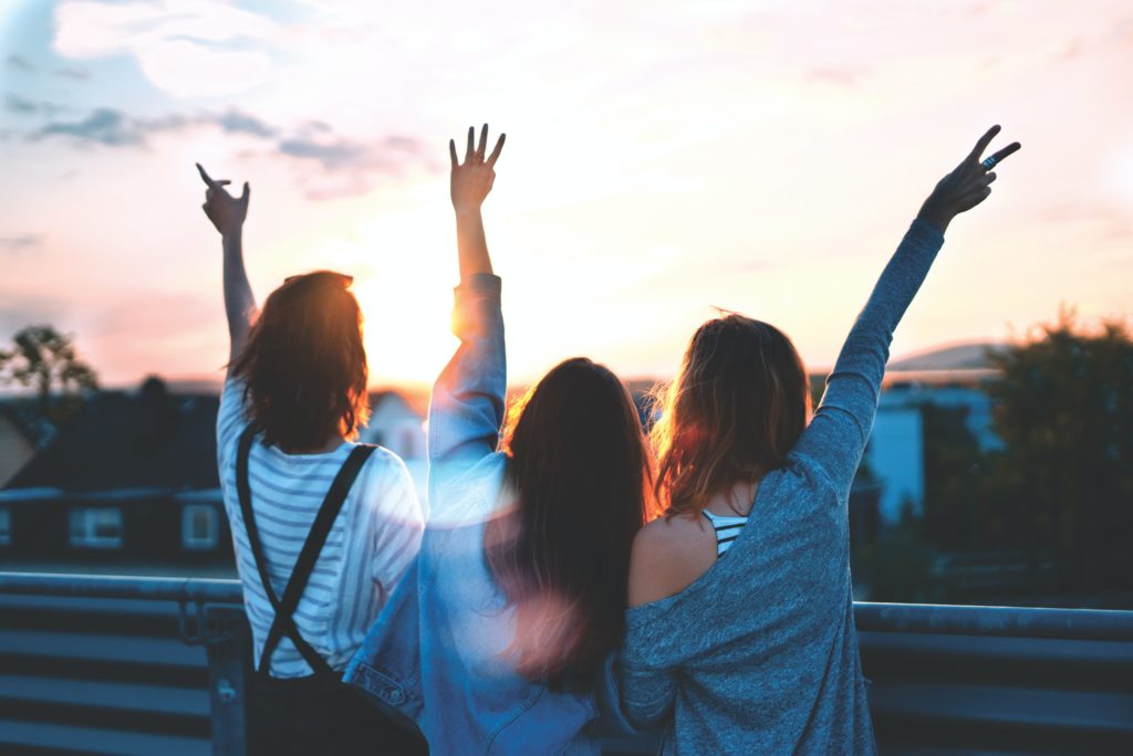photo of three friends with their hands in the air in front of a sunset from unsplash