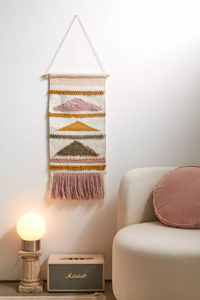 Woven wall hanging from Urban Outfitters with geometric shapes in light pink, orange, and olive green on a cream base