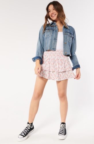 Hollister ruffled mini skirt in pink floral print paired with a white crop top, cropped denim jacket and black converse high tops
