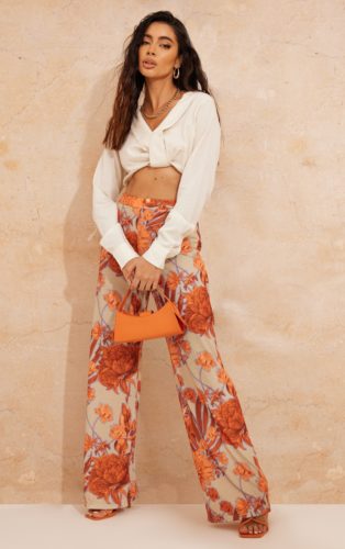 A cream top, orange floral wide leg trousers and an orange shoulder bag.