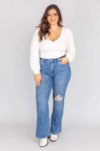 Cute plus size outfit with medium wash flares, cute white top, and white boots
