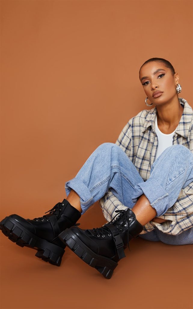 Photo of a woman sitting down and wearing a flannel shirt, rolled up jeans, a white tee, and chunky black combat boots