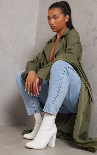 A green trench coat, light wash denim jeans and white ankle boots.
