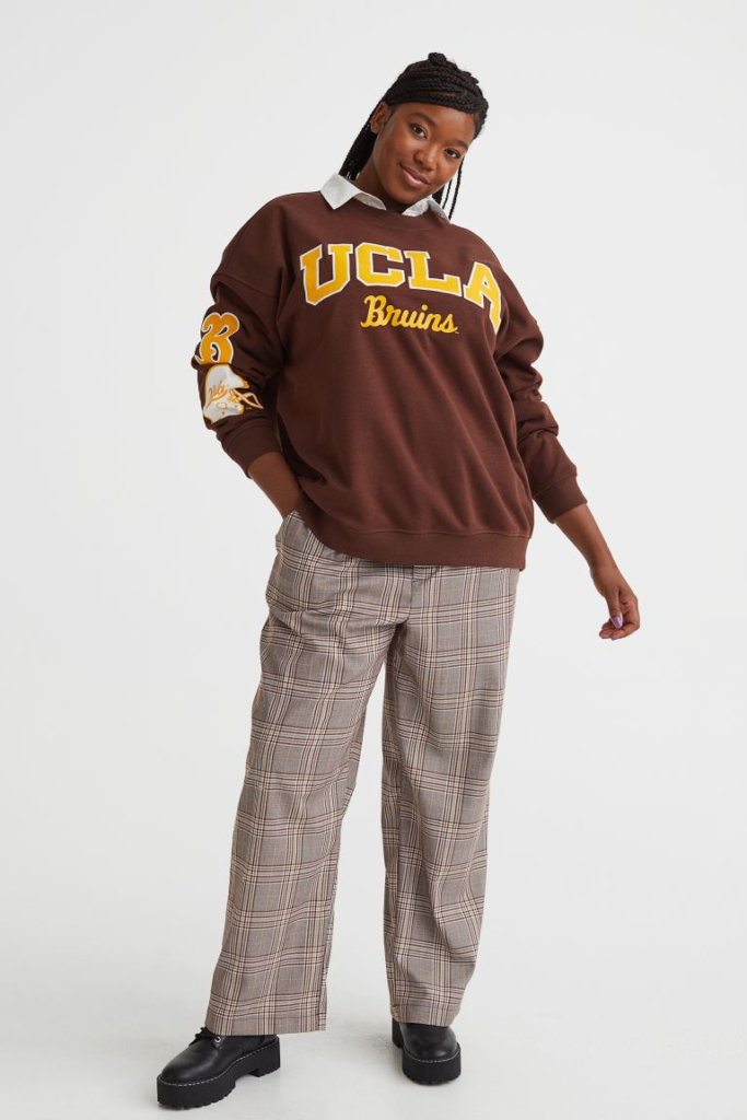 Plus size woman wearing brown plaid pants and a brown and yellow UCLA bruins sweatshirt