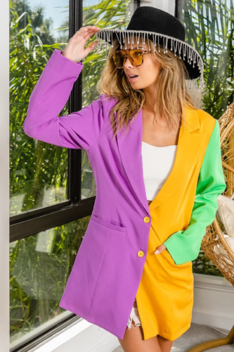 Woman wearing a mardi gras colored blazer over a white crop top with a fringed hat and denim shorts