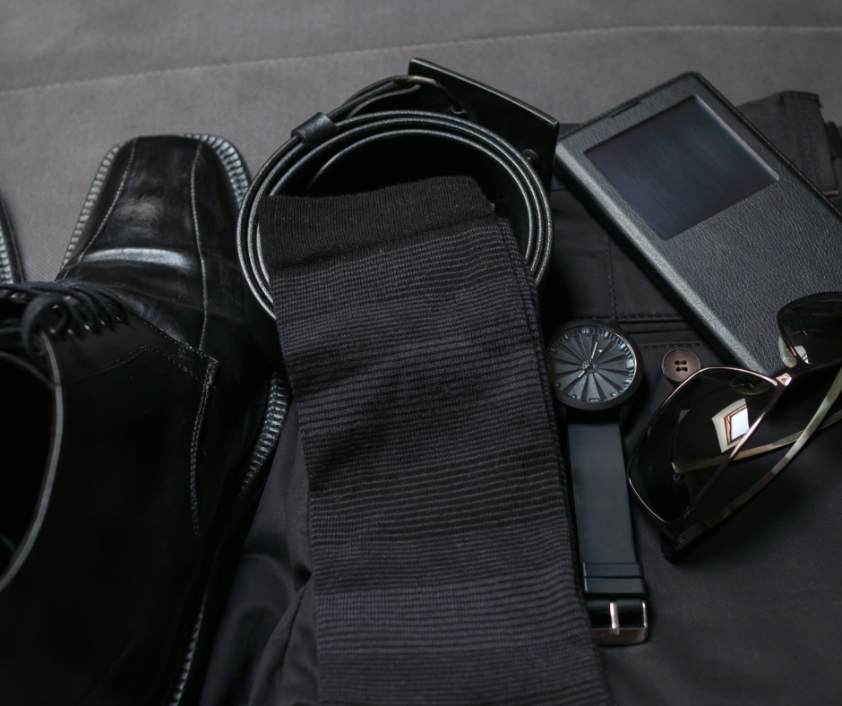 An assortment of mens accessories laid out, including shoes, a belt, a tie, sunglasses, and a watch